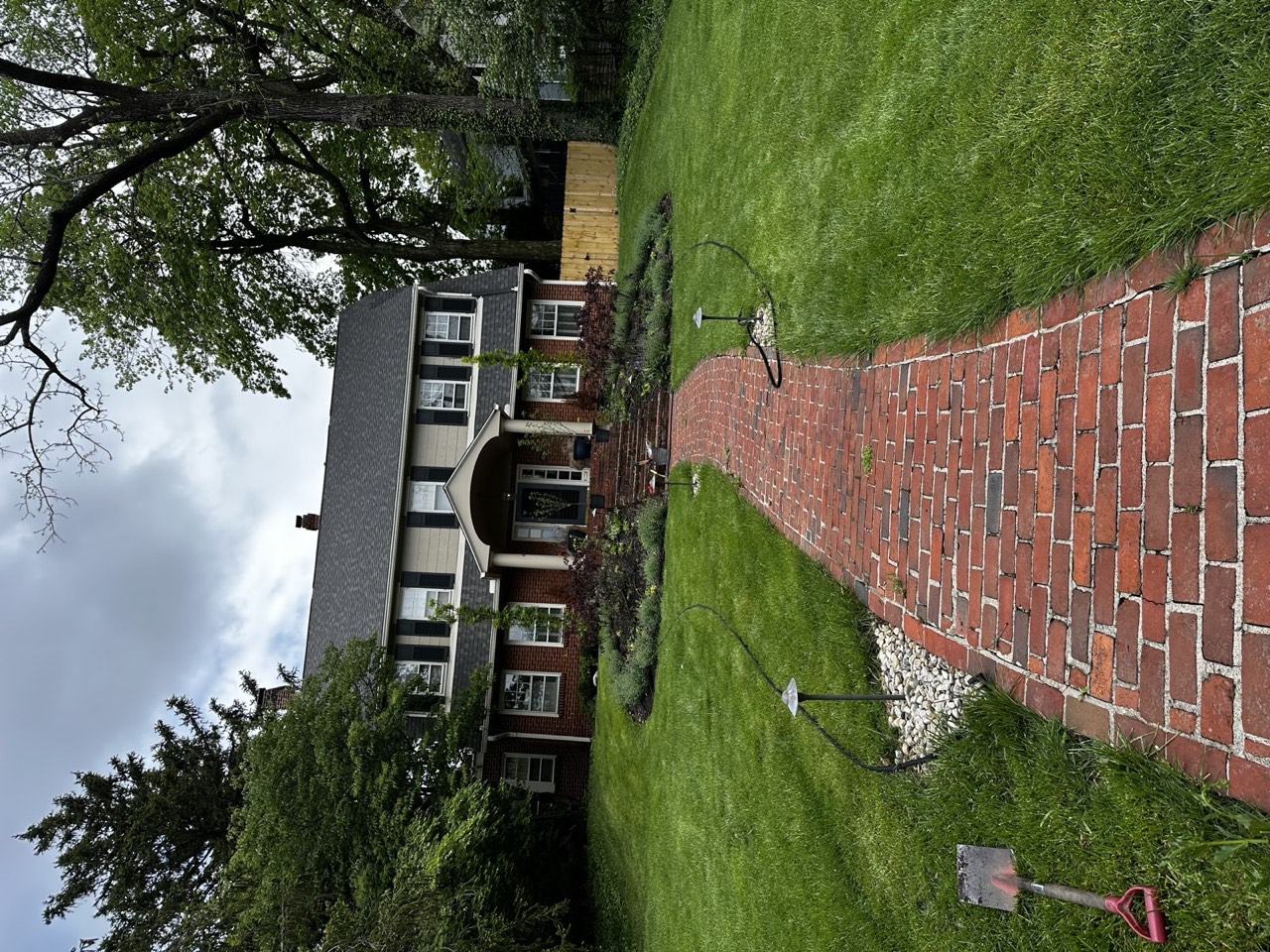 Front yard before the rework: thin foundation beds, a tired lawn, and a shovel and hose left out